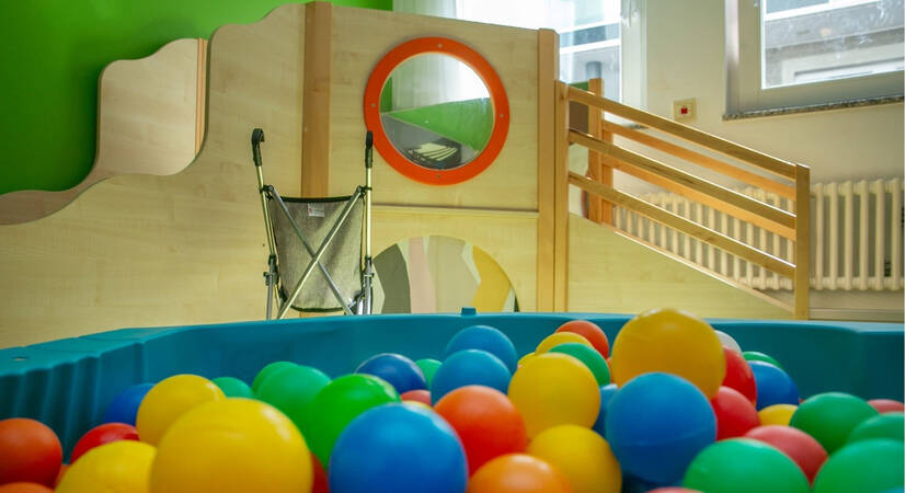 Ein farbenfrohes Bällebad in einem Spielzimmer mit einem hölzernen Spielgerüst und einer Rampe im Hintergrund.
