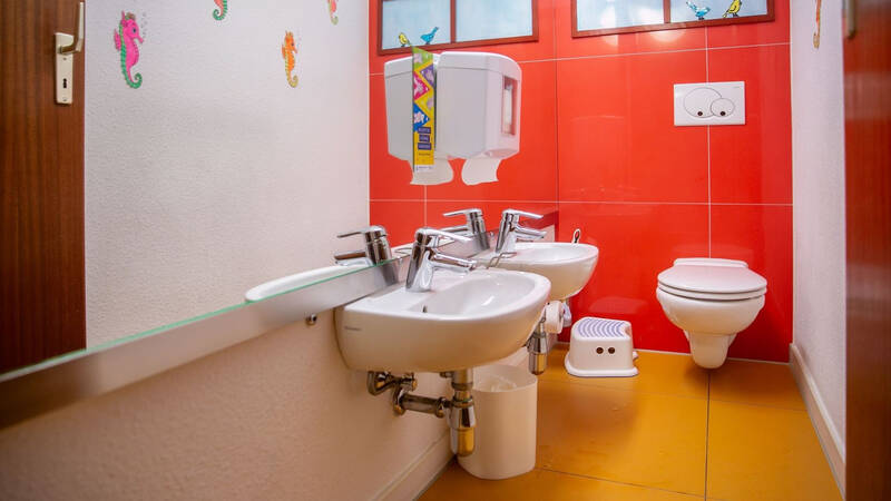 Ein Kinderbadezimmer mit roter Wandfarbe und zwei niedrigen Waschbecken, dazu kindgerecht gestaltete Accessoires wie bunte Wanddekorationen.